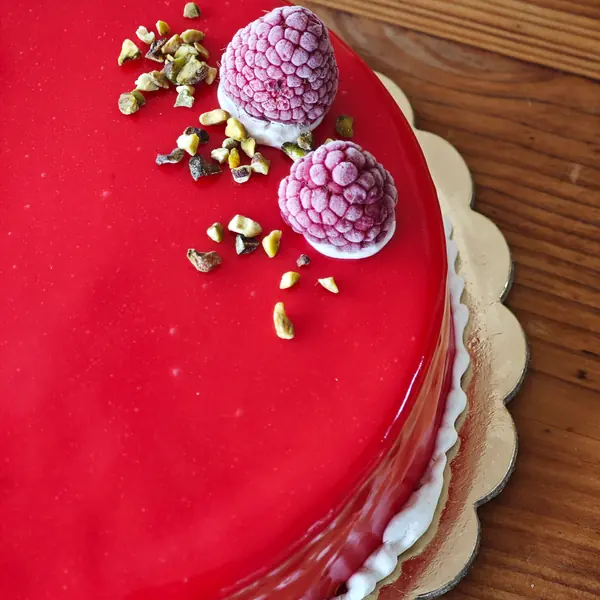 Una torta dalla glassa rossa lucida, con lamponi e granella di pistacchio