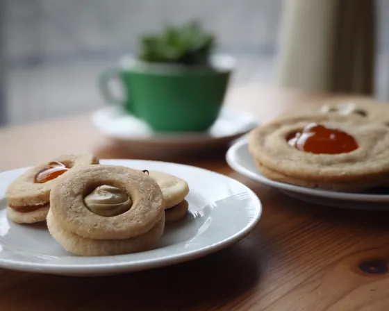 Biscotti ripieni di marmellata su due piattini, con una tazza verde sul tavolo del bar