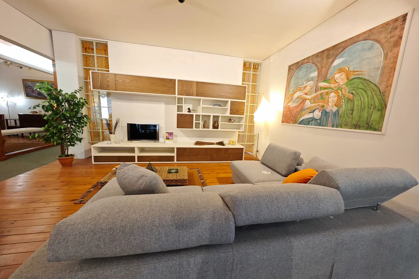 Un soggiorno dello showroom: parete attrezzata in legno e bianco, un grande divano grigio e un affresco alla parete