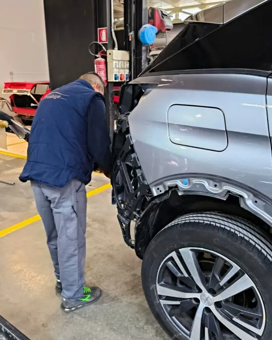 Un carrozziere chino sulla fiancata di un'auto grigia, smontata attorno al passaruota