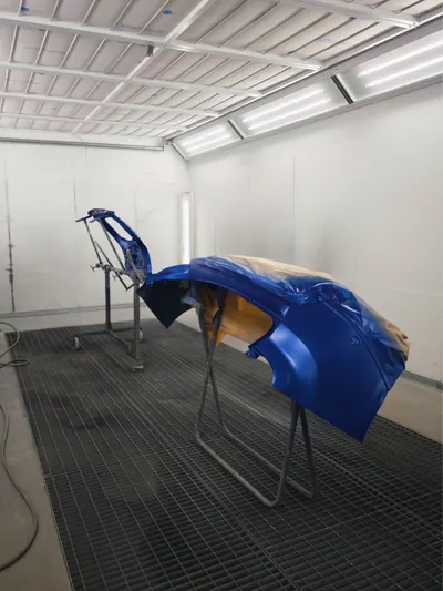 Un paraurti blu sul cavalletto, al centro del forno di verniciatura