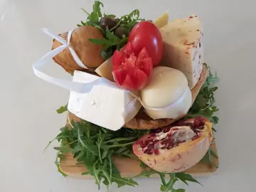 Formaggi freschi, pane, pomodoro e melagrana su un letto di rucola