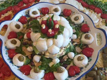 Un vassoio di nodini di mozzarella con pomodorini, olive e basilico