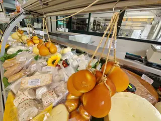 Scamorze appese sopra i formaggi del bancone, con un girasole