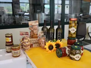 Miele, amaretti, vino, olio e conserve su un tavolo giallo, con due girasoli