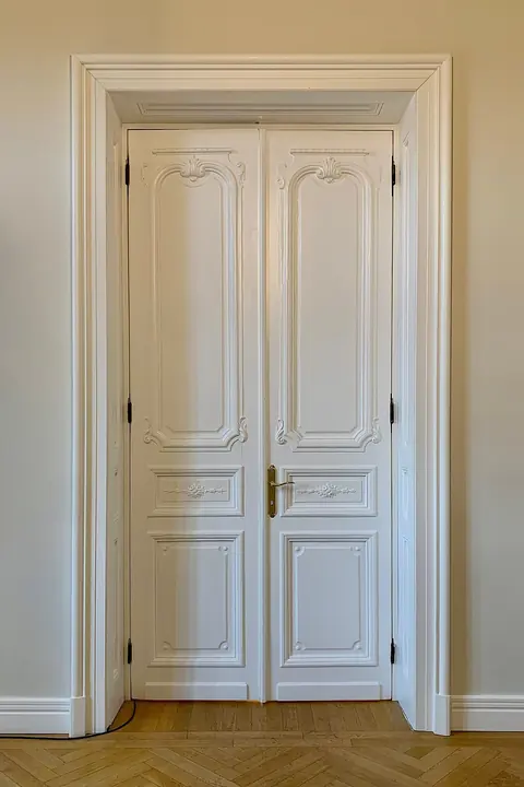 Una porta bianca a due ante con le modanature, in una stanza con il parquet