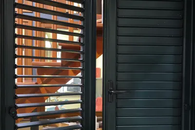 Una persiana verde scuro nello showroom: un’anta con le lamelle aperte, l’altra chiusa con la maniglia