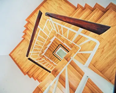 Scala in legno a pianta quadrata vista dall’alto, con la ringhiera bianca