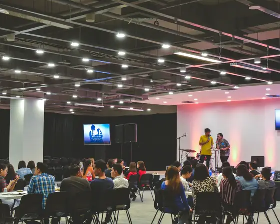 Una sala conferenze piena di gente, con due schermi e il palco illuminato