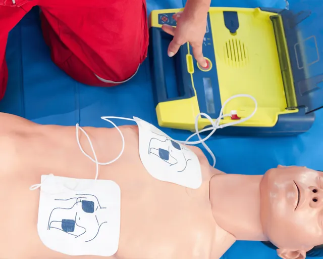 Un defibrillatore da addestramento acceso accanto a un manichino, con le piastre applicate sul petto