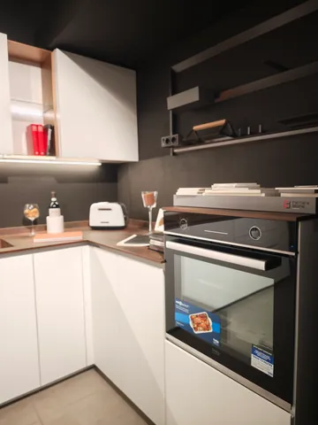 Cucina bianca ad angolo con forno a incasso e mensole scure a vista