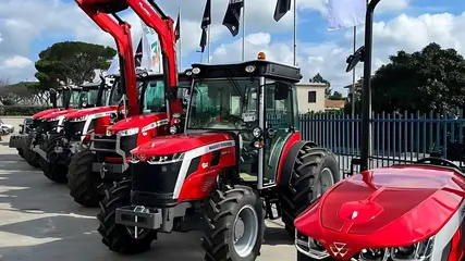 Trattori rossi con il caricatore frontale, in fila lungo la recinzione