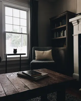 Una stanza in penombra con la poltrona accanto alla finestra e la libreria