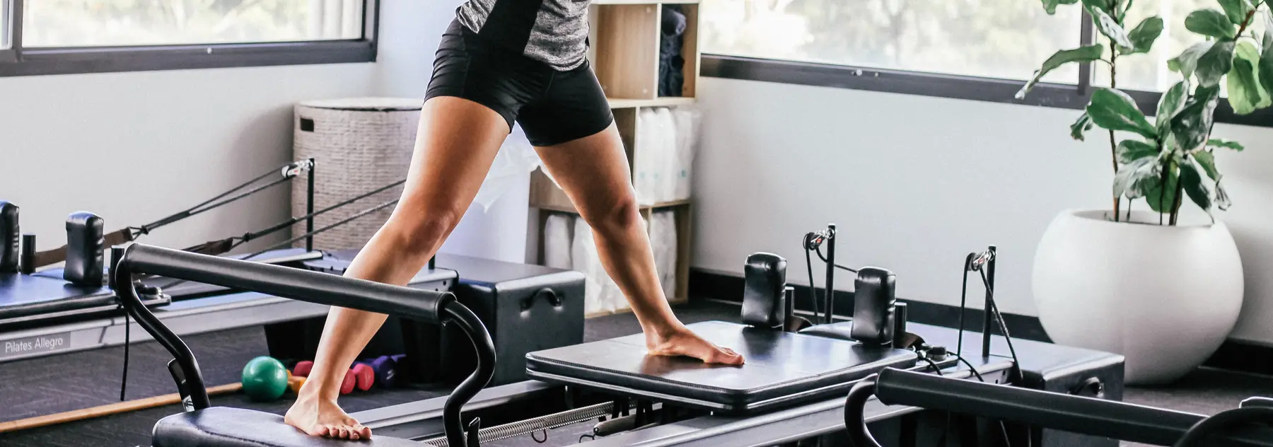 Le gambe di un'allieva in equilibrio su un reformer da Pilates, in una sala luminosa
