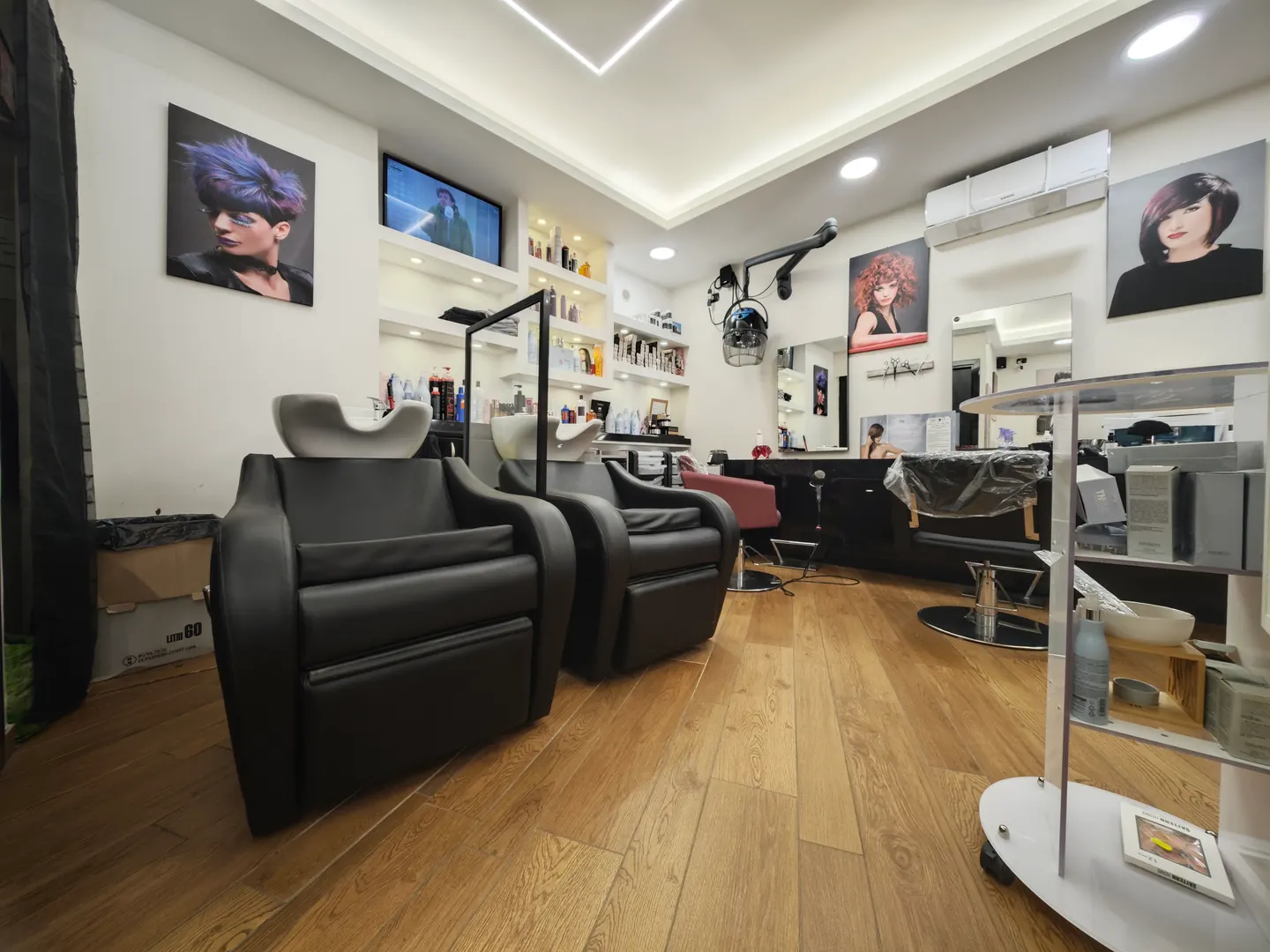 Il salone Life Color: due lavatesta in pelle nera, il parquet, le mensole dei prodotti e i ritratti alle pareti
