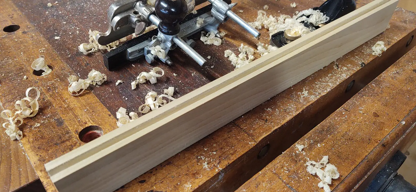Un banco da falegname coperto di trucioli, con una pialla e un listello di legno appena scanalato