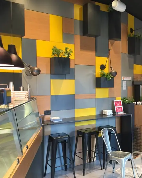 Un bar con la parete a riquadri gialli, grigi e in legno, il banco e gli sgabelli neri