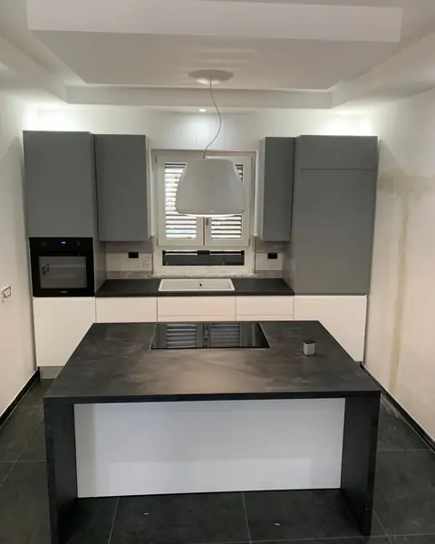 Una cucina bianca e grigia con l’isola dal piano nero, sotto un controsoffitto illuminato