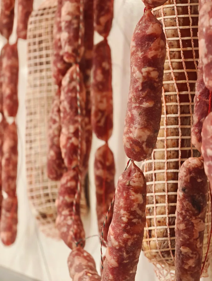 Salame a fuoco in primo piano tra altri appesi sfocati