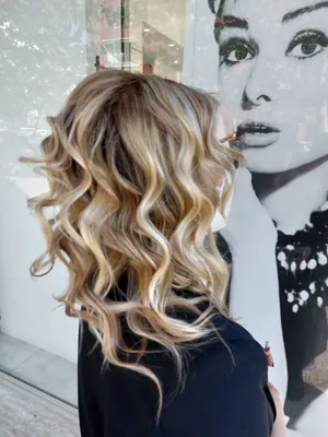 Onde bionde con balayage, di spalle davanti alla vetrina del salone
