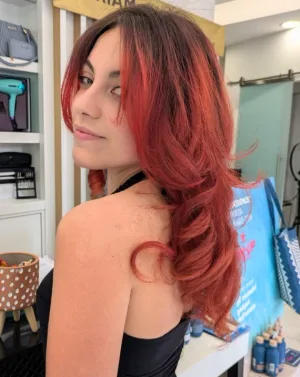 Una cliente di spalle si volta sorridendo, con i capelli lunghi e mossi color rame, nel salone