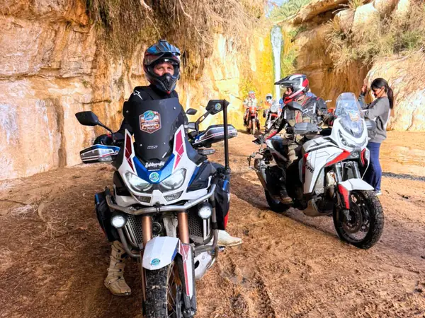 Motociclisti con le loro moto da viaggio su una pista di terra rossa, sotto una parete di roccia