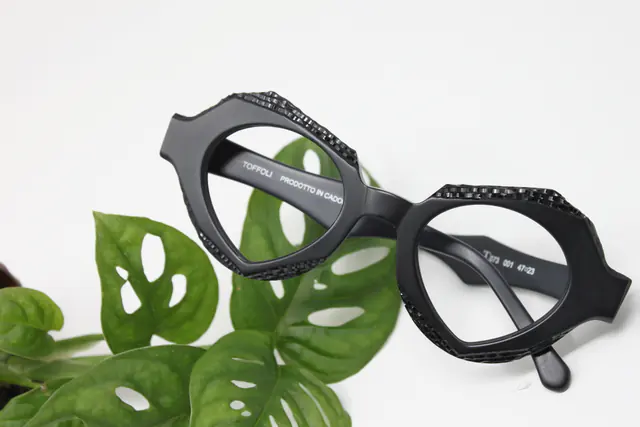 Montatura nera sfaccettata di Costantino Toffoli, fra le foglie di una monstera