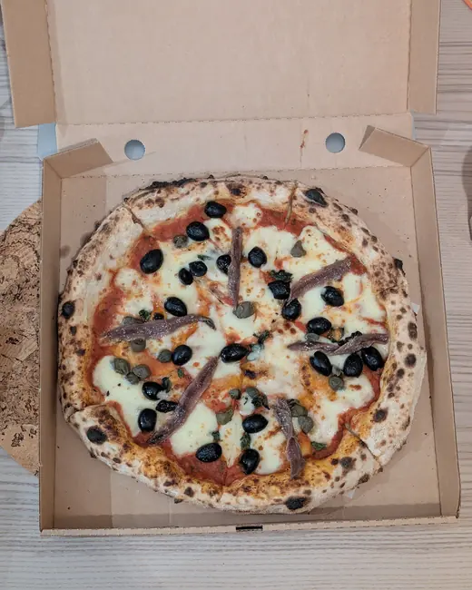 Una pizza napoletana con olive, alici e capperi nel cartone da asporto