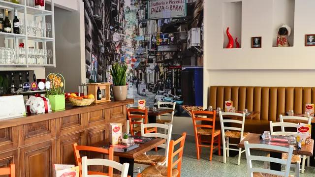 La sala: il bancone di legno con le bottiglie, il murale del vicolo e i tavoli apparecchiati