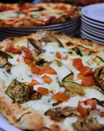 Pizza bianca con zucchine e melanzane grigliate e pomodorini, sulla pila dei piatti