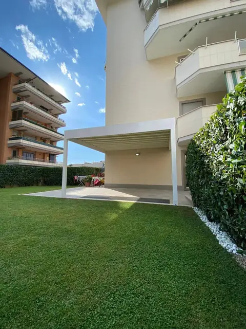 Una pergola bianca sul prato di un condominio, sotto il cielo azzurro