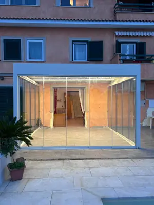 Pergola chiusa da vetrate panoramiche, illuminata la sera, davanti a una casa