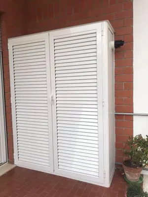 Armadio da esterno bianco con ante a persiana, su un balcone in mattoni