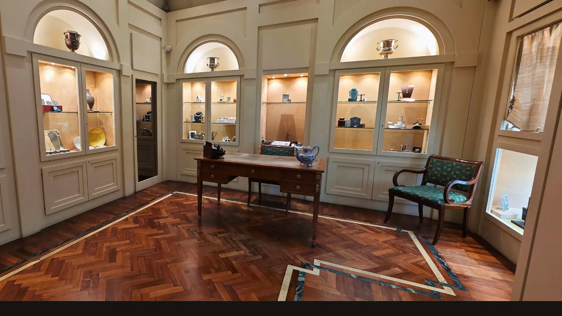 L'interno della gioielleria: vetrine ad arco illuminate, una scrivania antica e poltroncine di velluto verde