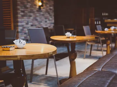 La sala di un locale con tavolini tondi in legno, sedie e divanetto in pelle