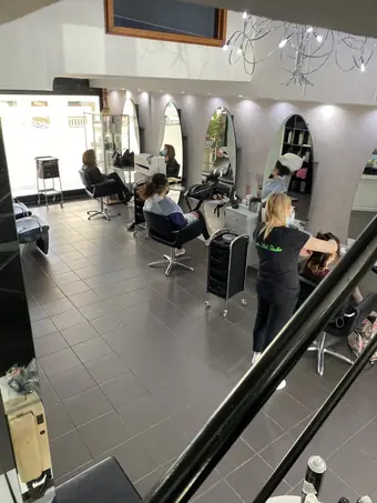 Una parrucchiera al lavoro fra le postazioni, vista dalla scala
