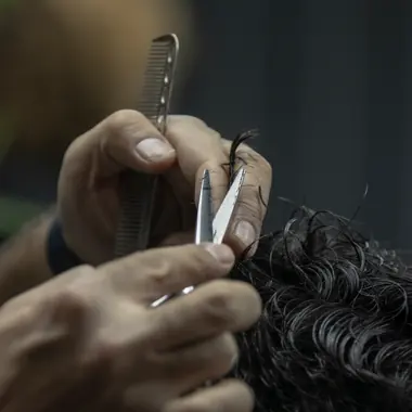 Le mani del parrucchiere, con pettine e forbici, accorciano una ciocca di capelli scuri e mossi
