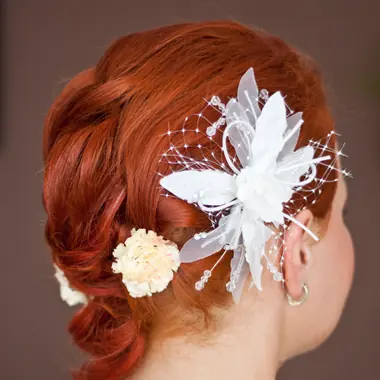 Una sposa di spalle, con i capelli rossi raccolti e un fiore bianco fra i capelli