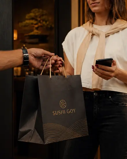 Una busta nera con il logo di Sushi Goy passa dalla mano del fattorino a quella di una cliente