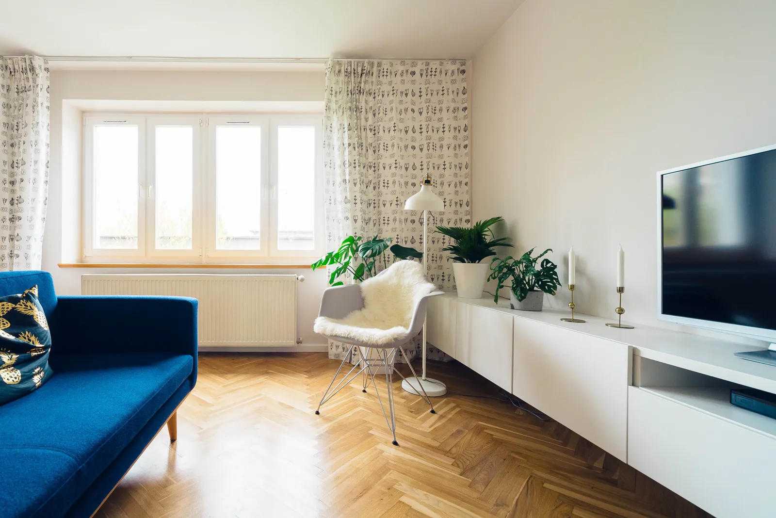 Un soggiorno luminoso con le tende a fantasia alla finestra, un divano blu e il parquet a spina di pesce