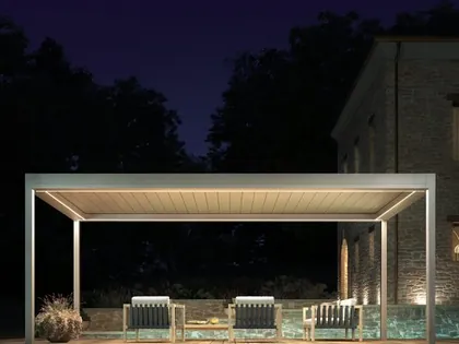 Una pergola bioclimatica illuminata di sera, sopra un salotto da esterno