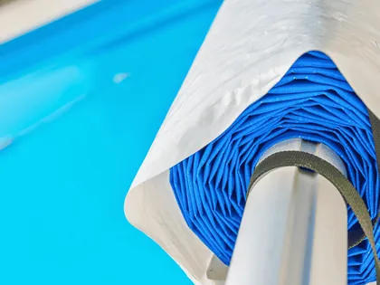 Il telo di copertura di una piscina arrotolato sul suo rullo, sopra l’acqua azzurra